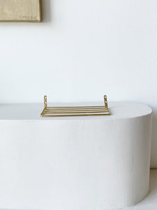 flat railed brass wire shelf on white pedestal