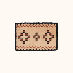 small tan rug with orange and black geometric designs in shaggy yarn lying