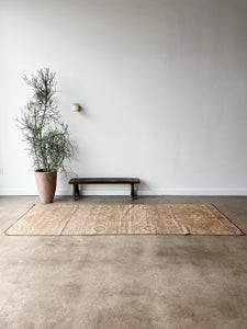 emily vintage turkish three feet seven inch by nine foot seven inch rug lying on cement floor in front of tall plant and bench