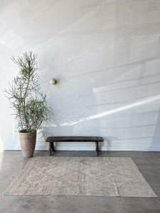 light tan and terracotta vintage turkish rug lying on cement floor in front of a tall plant and bench