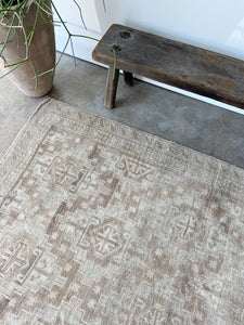 light tan and terracotta vintage turkish rug lying on cement floor in front of a tall plant and bench
