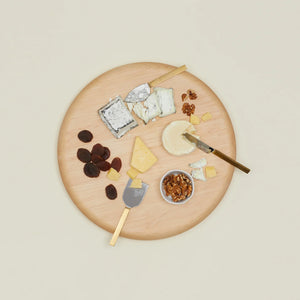 set of three two-toned cheese knoves being used to cut cheese on a round wooden charcuterie platter with fruit and nuts