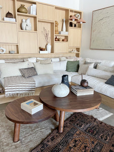 a pair of nesting Nichoir Coffee Tables shown styled with books and ceramics on top of rugs and in front of a sofa with pillows 
